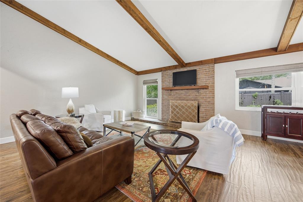 A living room features a brick fireplace, vaulted ceiling with wood beams, and wood flooring — 8080 NW 47TH STREET, OCALA, FL