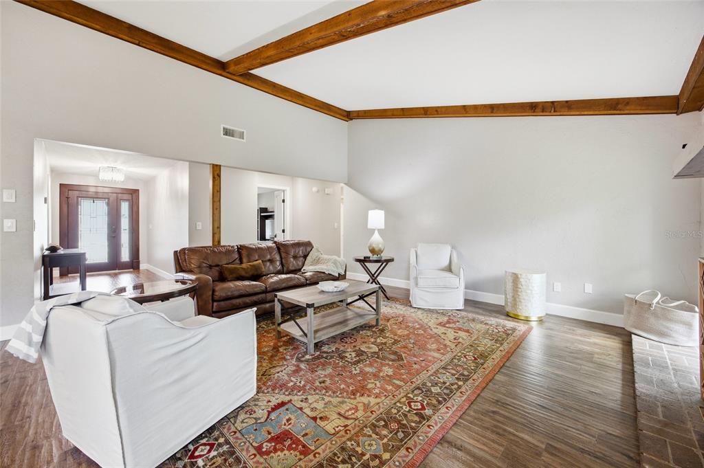 A living room features wood ceiling beams, a patterned area rug, and wood-look flooring — 8080 NW 47TH STREET, OCALA, FL