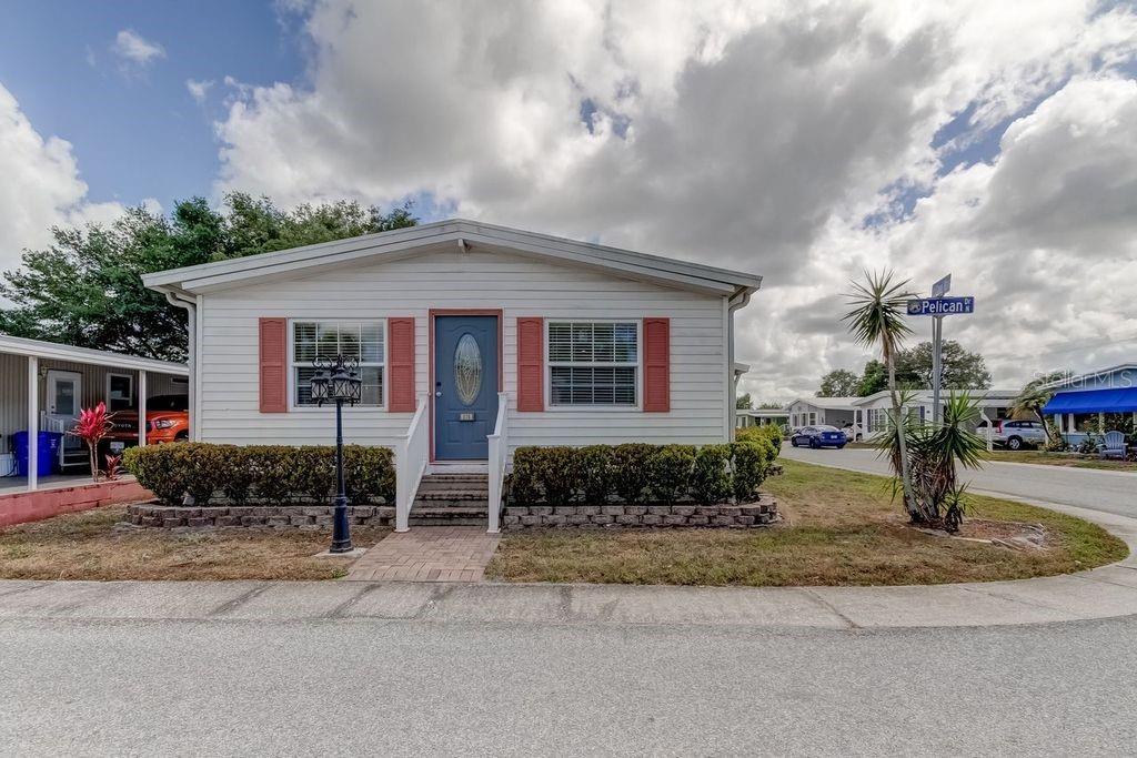 A single-story manufactured home with white siding, red shutters, and a blue front door — 278 PELICAN DRIVE N, OLDSMAR, FL