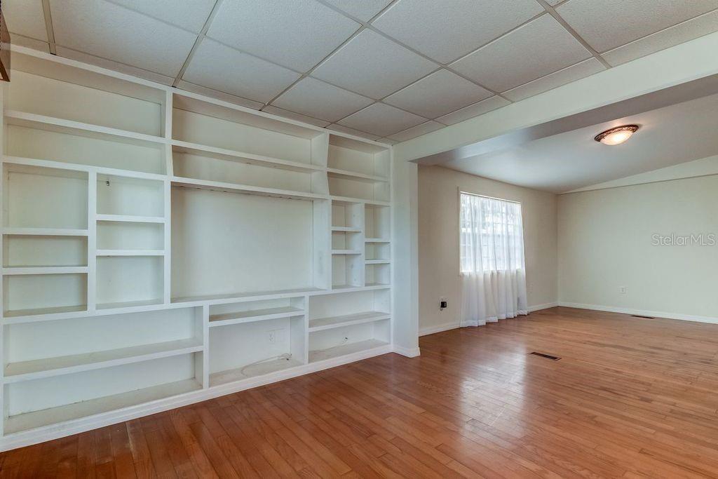 A room with hardwood floors, a large built-in white shelving unit, and a drop ceiling — 278 PELICAN DRIVE N, OLDSMAR, FL