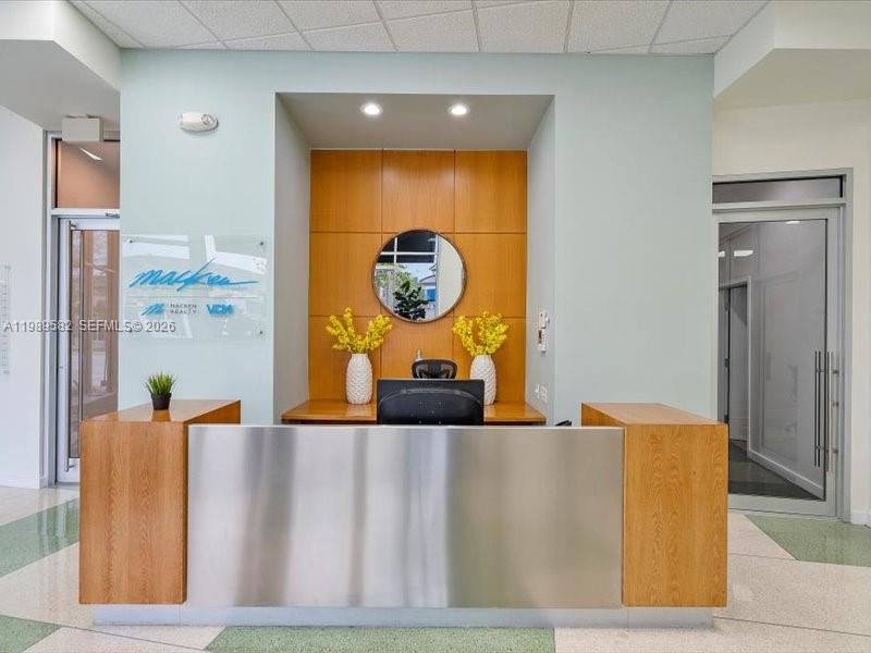 A modern reception area features a wood and metal desk, yellow floral arrangements, and signage — 2404 Hollywood Blvd, Hollywood FL 33020, HOLLYWOOD, FL