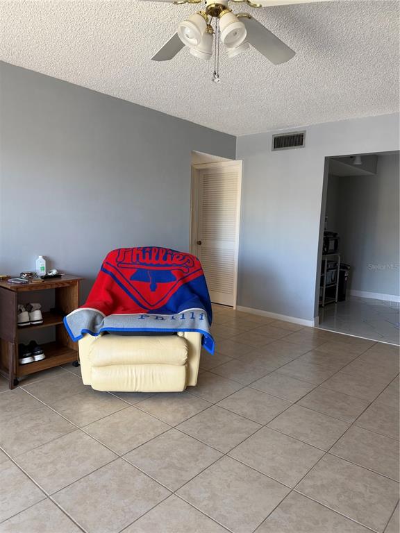 A living room features a beige recliner with a Phillies blanket and tiled flooring — 2688 PINE RIDGE WAY N UNIT A2, PALM HARBOR, FL