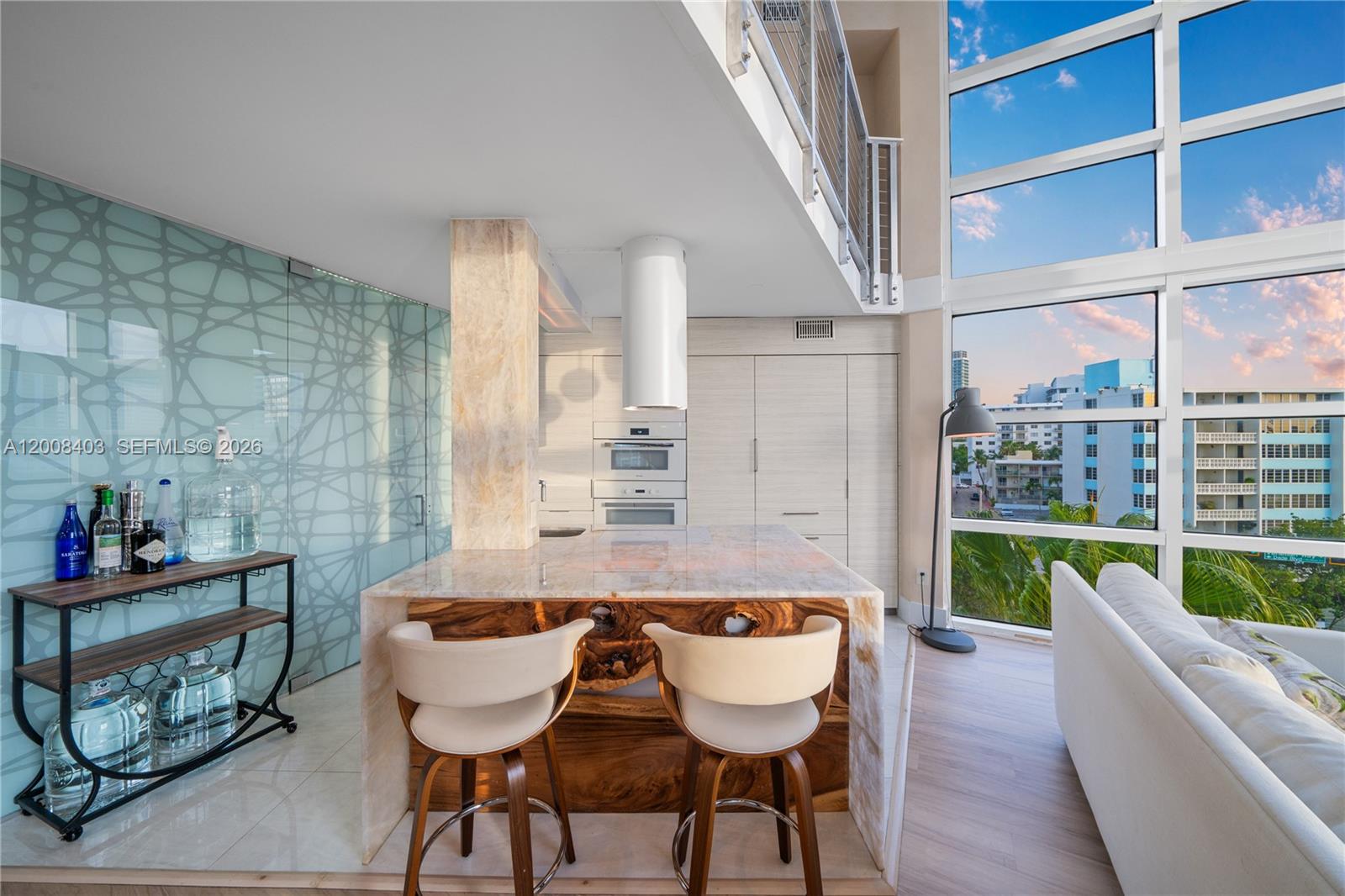 A modern kitchen features a stone-topped island with wood accents, bar stools, and floor-to-ceiling windows — 1701 Sunset Harbour Dr # L501, Miami Beach FL 33139, MIAMI BEACH, FL