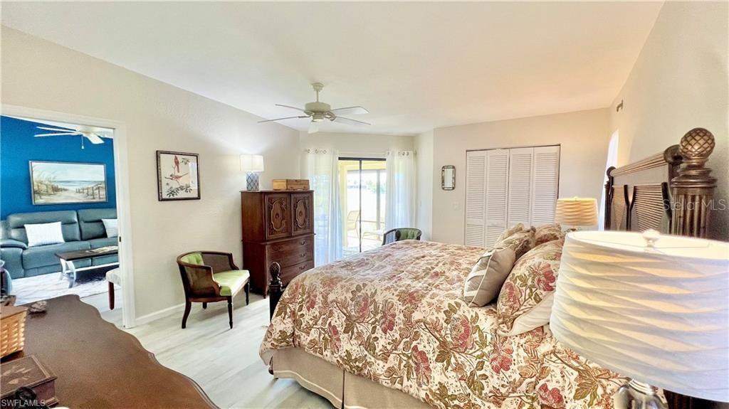 A bedroom with a floral bedspread, wooden dresser, and an adjacent living area with blue walls — 1640 ATARES DRIVE UNIT 31, PUNTA GORDA, FL