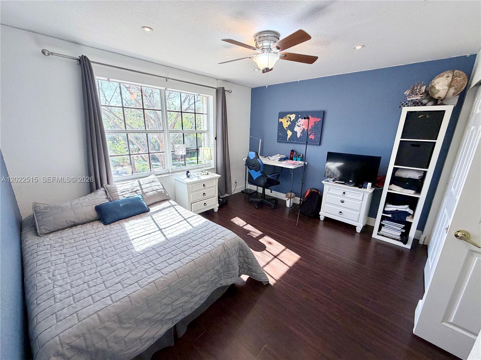 A bedroom features dark wood flooring, a blue accent wall, and a bed with gray bedding — 4020 Sapphire Cv, Weston FL 33331, WESTON, FL