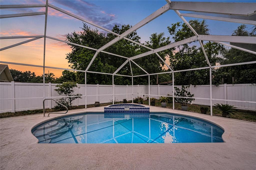 A swimming pool and attached spa are enclosed within a white screened lanai at sunset — 2508 14TH AVENUE W, BRADENTON, FL