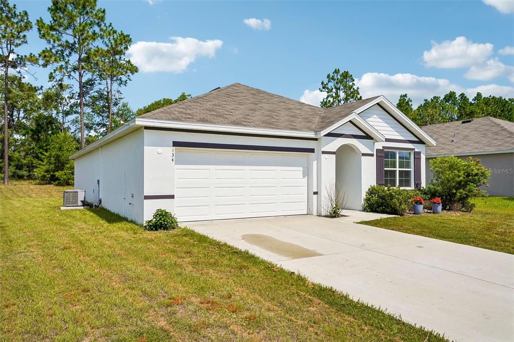 A single-story house with a white stucco exterior, a two-car garage, and a concrete driveway — 134 HICKORY COURSE TRAIL, OCALA, FL