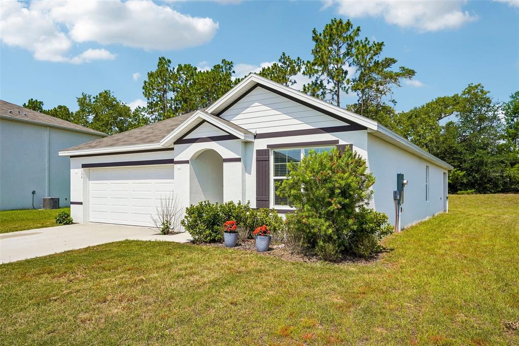 A single-story white house with a two-car garage and dark trim sits on a lawn — 134 HICKORY COURSE TRAIL, OCALA, FL
