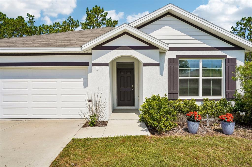 A single-story house with a white stucco facade, dark brown trim, and a two-car garage — 134 HICKORY COURSE TRAIL, OCALA, FL
