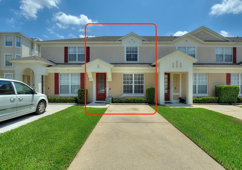 A two-story townhouse exterior with a red front door, a concrete driveway, and green lawn — 8106 PRINCESS PALM LANE, KISSIMMEE, FL