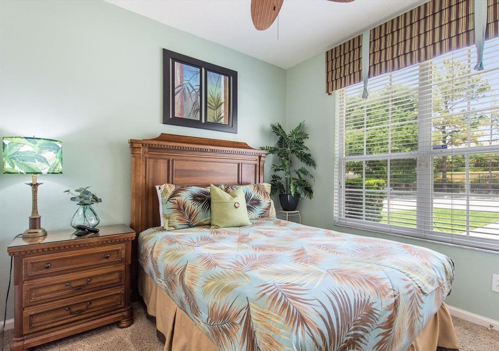 A bedroom features a wooden bed frame, palm-print bedding, a nightstand, and a large window — 8106 PRINCESS PALM LANE, KISSIMMEE, FL