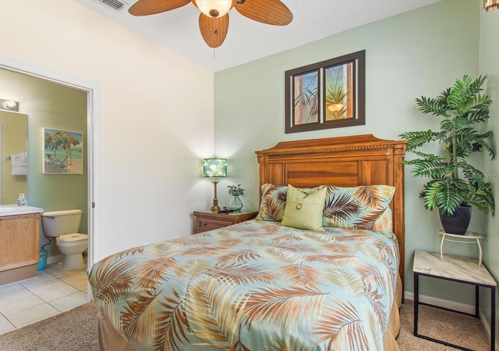 A bedroom with a wooden headboard, palm-patterned bedding, and an attached bathroom — 8106 PRINCESS PALM LANE, KISSIMMEE, FL