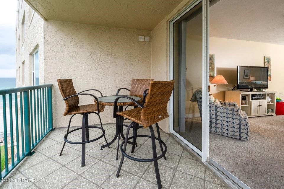 A balcony with a small table and three wicker chairs overlooks the ocean — 4575 S ATLANTIC AVENUE UNIT 6502, PORT ORANGE, FL
