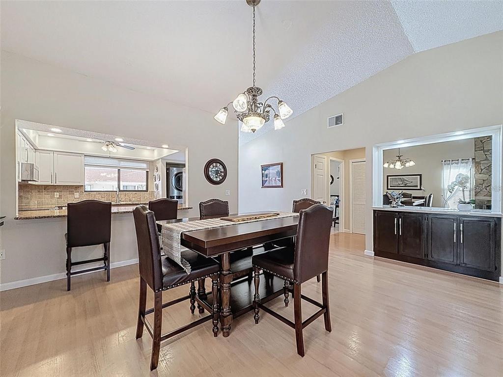 A dining area features a wooden table, leather chairs, a chandelier, and a kitchen pass-through — 9981 EAGLES POINT CIRCLE UNIT 4, PORT RICHEY, FL