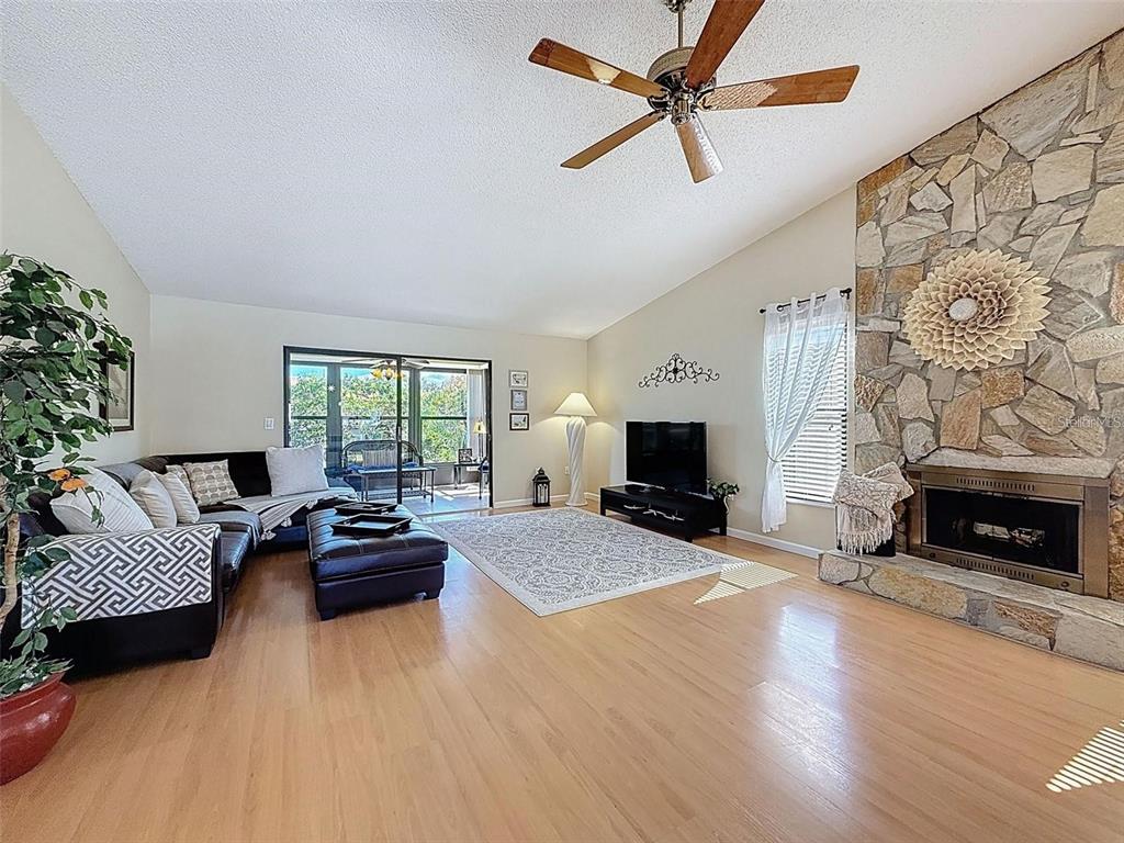 A living room features light wood floors, a stone fireplace, and a ceiling fan — 9981 EAGLES POINT CIRCLE UNIT 4, PORT RICHEY, FL