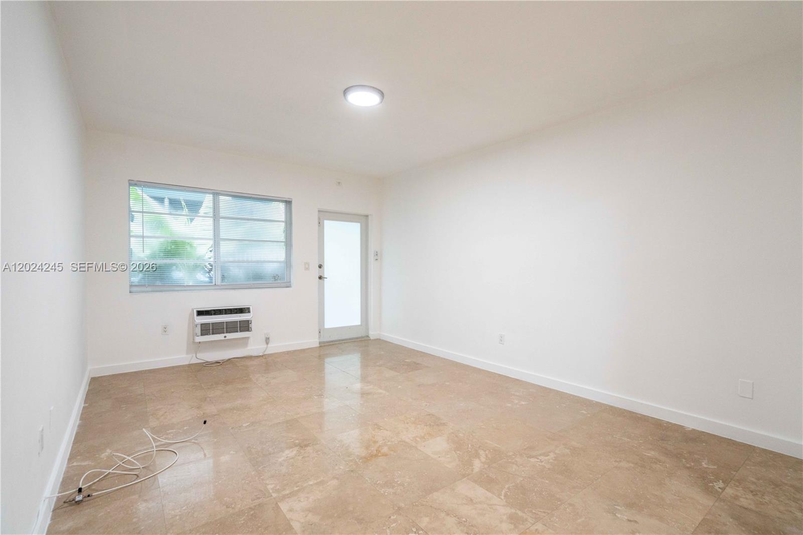 An empty room features white walls, beige tile flooring, a window, and a door — 1120 Euclid Ave # 6, Miami Beach FL 33139, MIAMI BEACH, FL