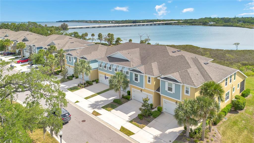 An aerial view shows a row of multi-story townhomes with garages near a large body of water — 9009 PALM KEY AVENUE, OLDSMAR, FL