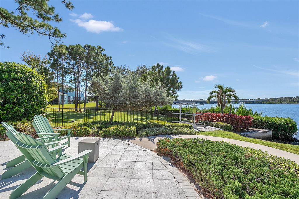 A paved patio with two Adirondack chairs overlooks a fenced lawn and a waterfront view — 9009 PALM KEY AVENUE, OLDSMAR, FL