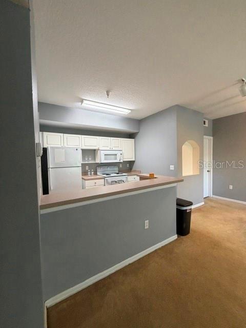 A kitchen with white cabinets and appliances features a breakfast bar overlooking a carpeted room — 5524 METROWEST BOULEVARD UNIT 206, ORLANDO, FL