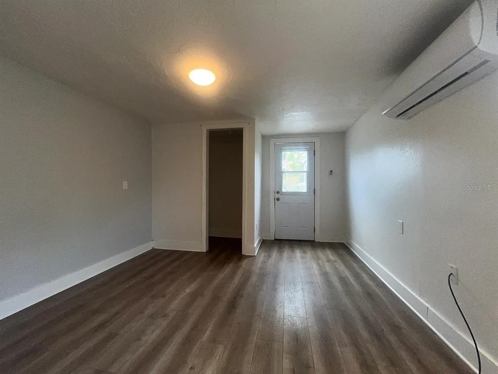 An empty room features light gray walls, wood-look flooring, a doorway, and a wall-mounted air conditioner — 1713 29TH STREET W, BRADENTON, FL