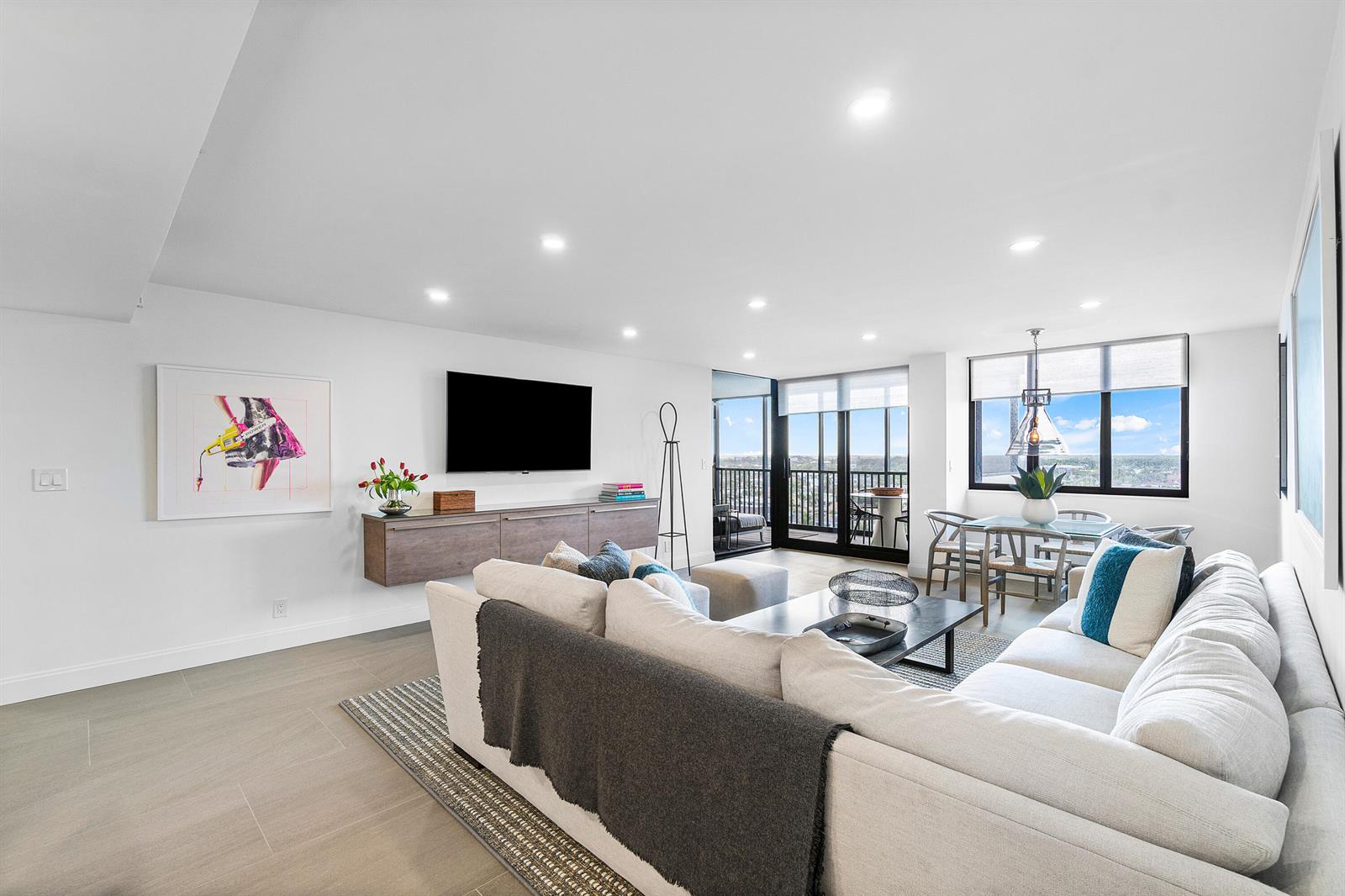 A modern living and dining area with a sectional sofa, wall-mounted console, and balcony access — 3420 S Ocean Boulevard # 14x, Highland Beach FL 33487, HIGHLAND BEACH, FL