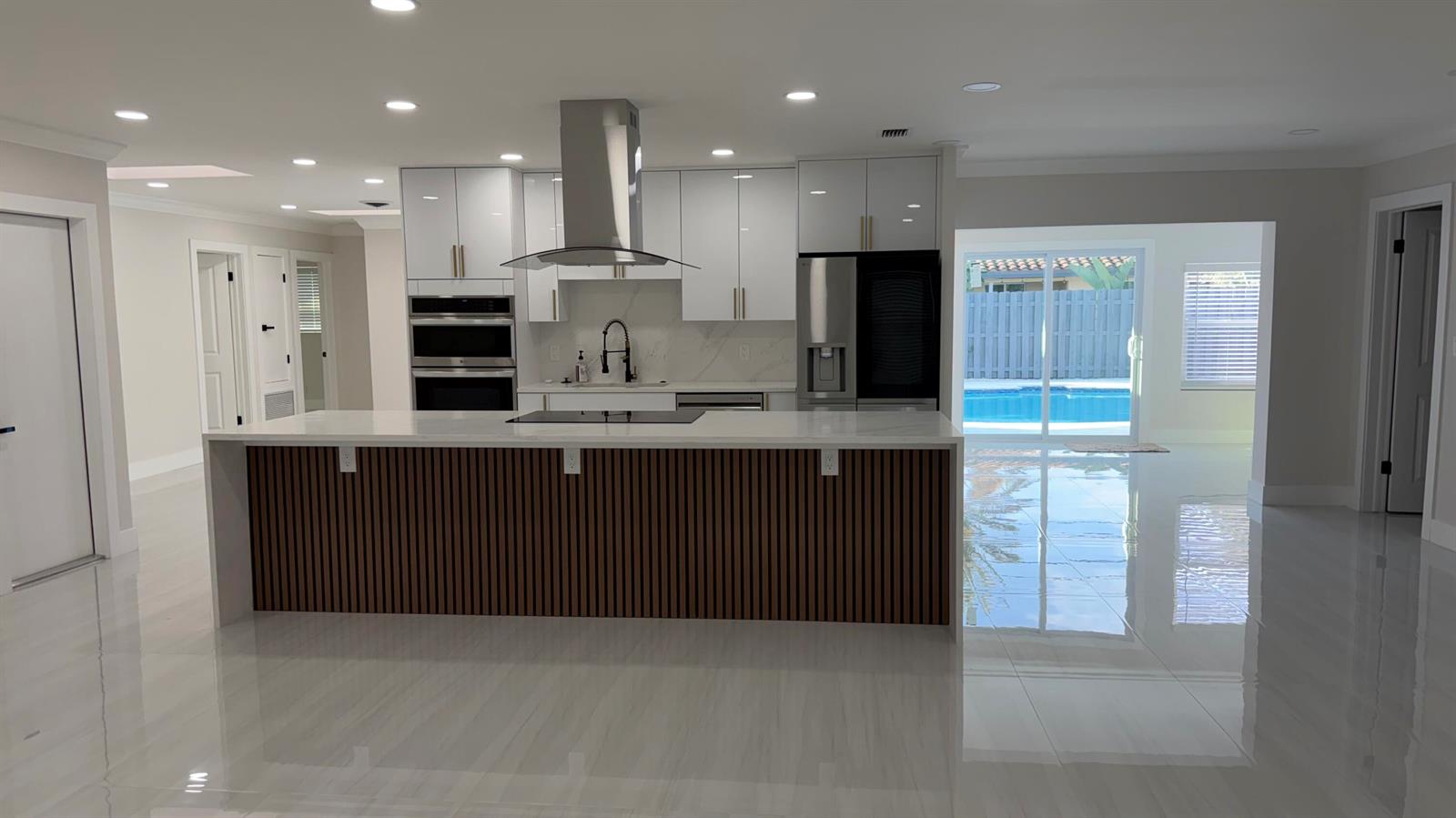 A modern kitchen features white cabinets, a slatted wood island, and a view of a pool — 2521 NE 45th Street, Lighthouse Point FL 33064, LIGHTHOUSE POINT, FL