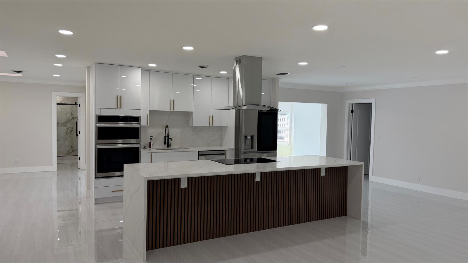 A modern kitchen features white glossy cabinets, a marble-topped island with wood slats, and stainless appliances — 2521 NE 45th Street, Lighthouse Point FL 33064, LIGHTHOUSE POINT, FL