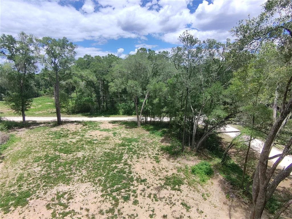 An elevated view of a cleared, sandy lot surrounded by mature trees and a road — SW 53RD PL, OCALA, FL