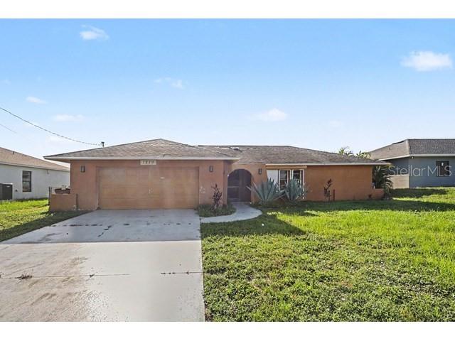 A single-story house with a tan stucco exterior, a two-car garage, and a concrete driveway — 1219 NE 14TH PLACE, CAPE CORAL, FL