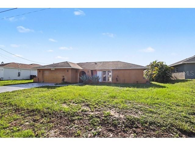 A single-story house with a tan stucco exterior and a large front yard — 1219 NE 14TH PLACE, CAPE CORAL, FL