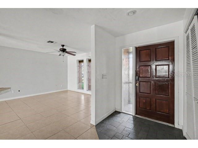 An entryway with a dark wood door leads into a tiled living area with a ceiling fan — 1219 NE 14TH PLACE, CAPE CORAL, FL