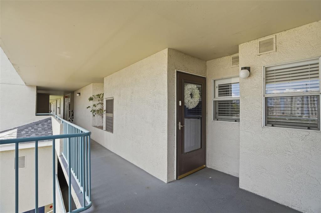 An outdoor apartment walkway features a brown front door with a wreath and blue railings — 5557 SEA FOREST DRIVE UNIT 215, NEW PORT RICHEY, FL