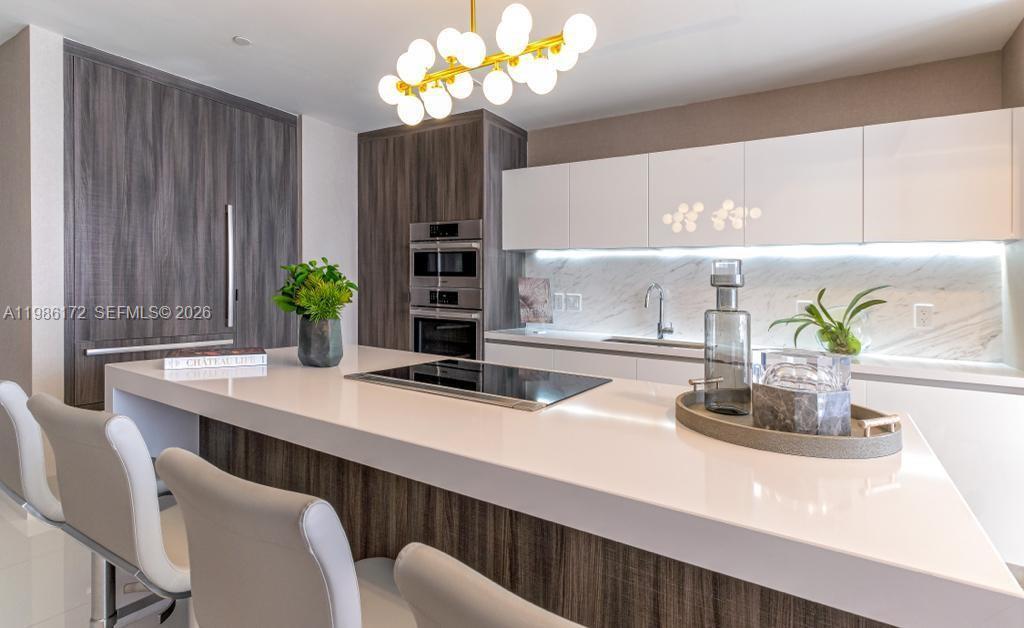 A modern kitchen features a large white island, dark wood cabinetry, and white upper cabinets — 851 NE 1st Ave # 1011, Miami FL 33132, MIAMI, FL