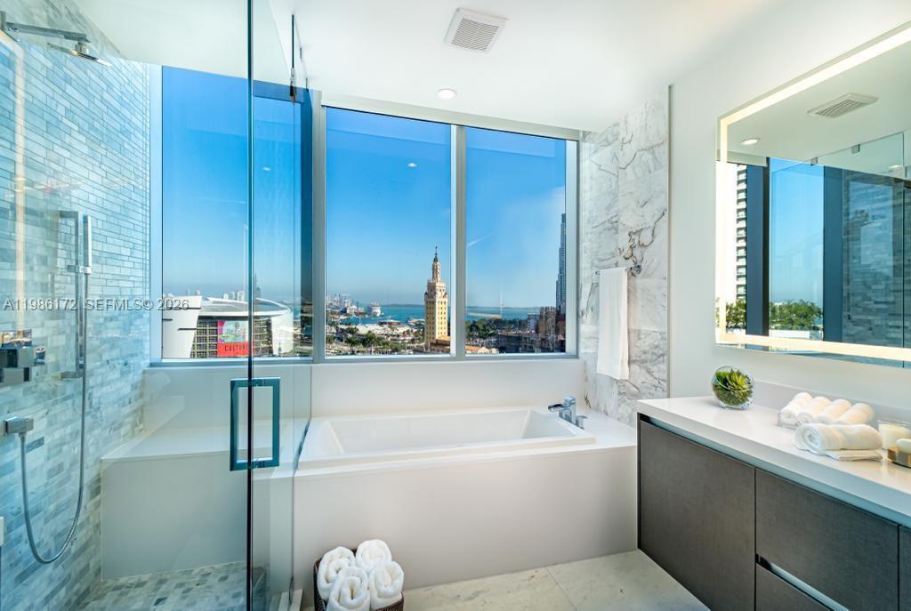 A modern bathroom features a soaking tub, glass-enclosed shower, and a view of the city — 851 NE 1st Ave # 1011, Miami FL 33132, MIAMI, FL