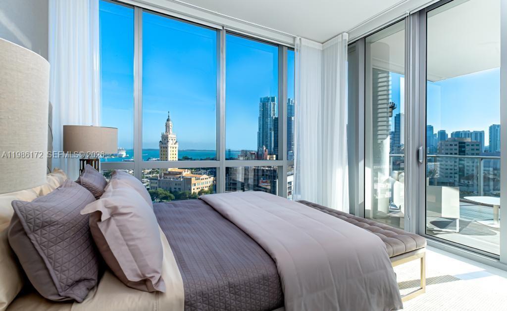 A bedroom with a large bed, floor-to-ceiling windows, and a view of city buildings — 851 NE 1st Ave # 1011, Miami FL 33132, MIAMI, FL