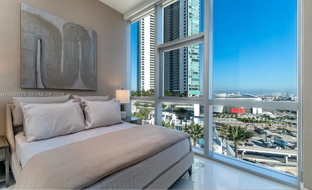 A bedroom with a bed and large windows overlooking a city skyline and stadium — 851 NE 1st Ave # 1011, Miami FL 33132, MIAMI, FL