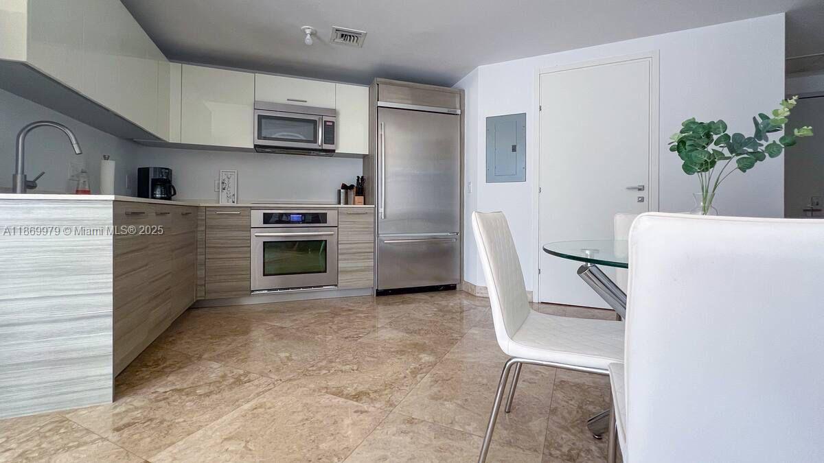 A modern kitchen features light wood cabinets, stainless steel appliances, and beige tile flooring — 1300 Brickell Bay Dr # 3007, Miami FL 33131, MIAMI, FL