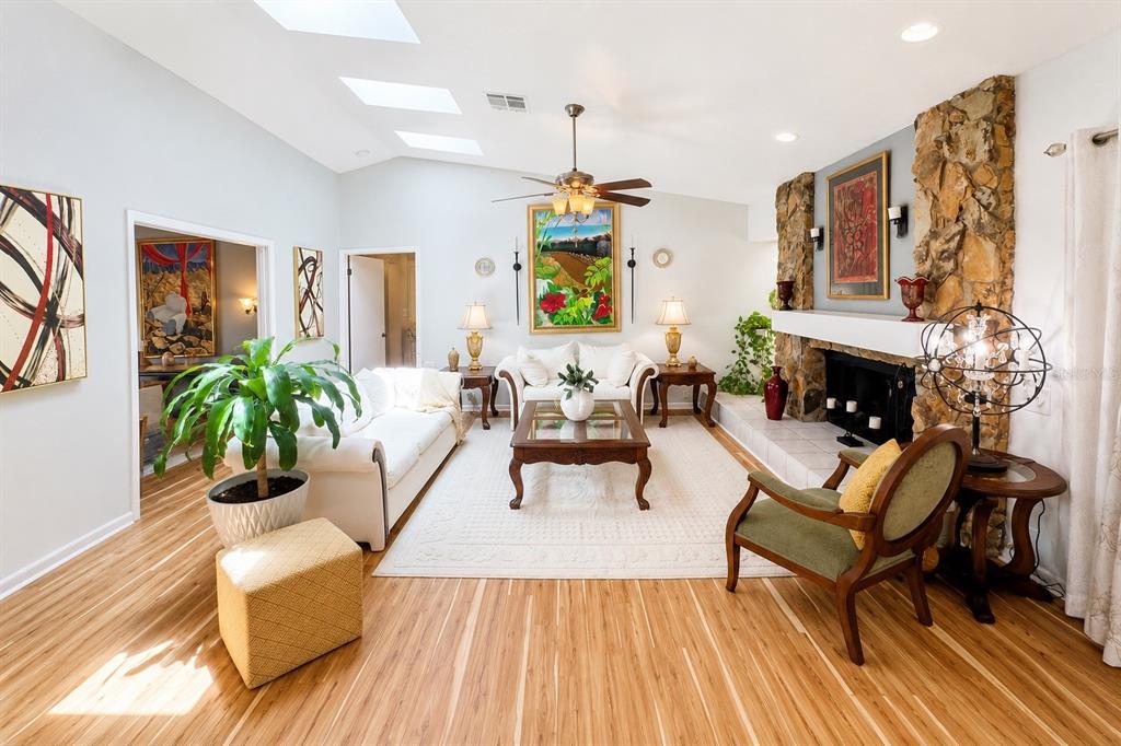 A living room features a stone fireplace, vaulted ceiling with skylights, and light wood flooring — 9801 DIDRIKSON DRIVE, NEW PORT RICHEY, FL