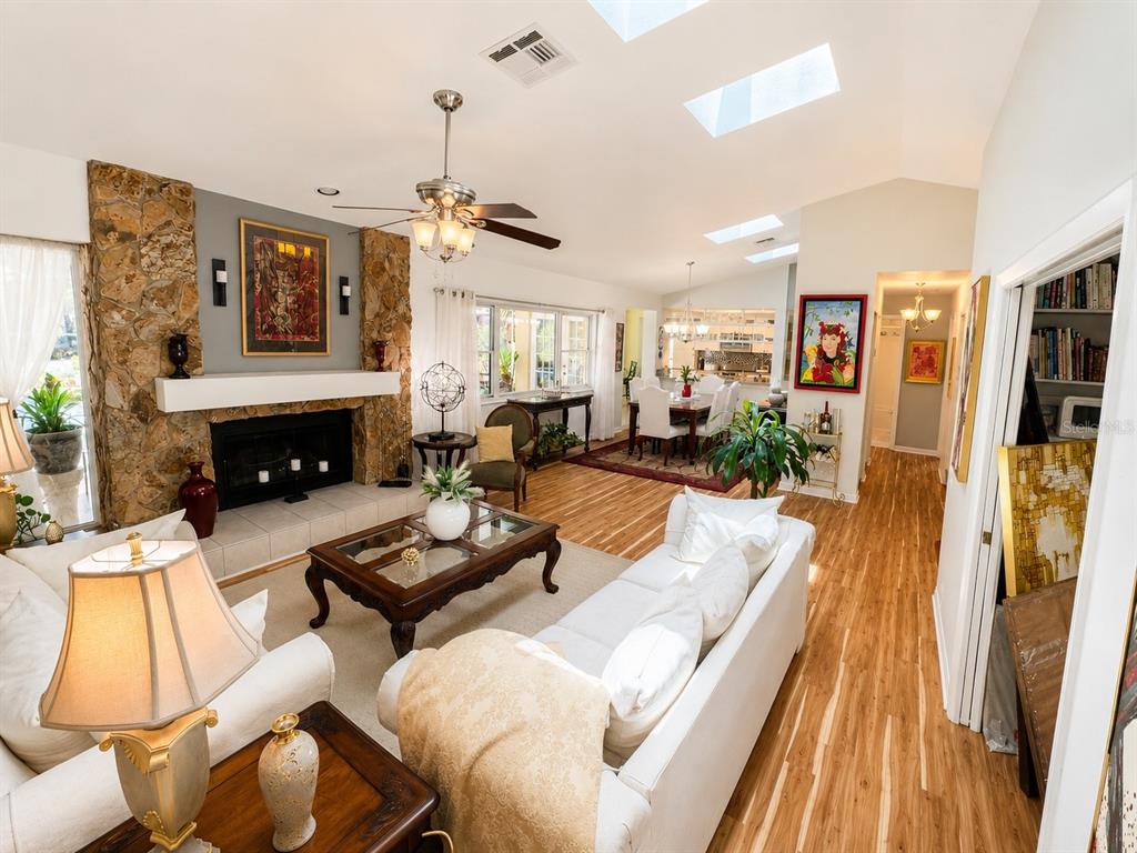 A living room with a stone fireplace, white sofas, wood flooring, and vaulted skylight ceilings — 9801 DIDRIKSON DRIVE, NEW PORT RICHEY, FL