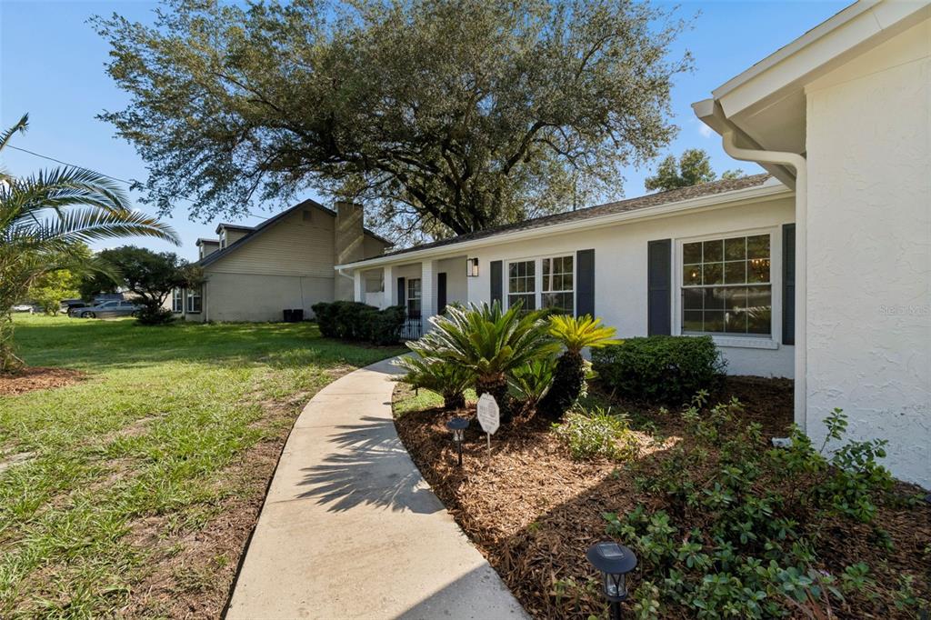 A concrete walkway leads to the front entrance of a white house with dark shutters — 507 ROLLINGVIEW DRIVE, TEMPLE TERRACE, FL