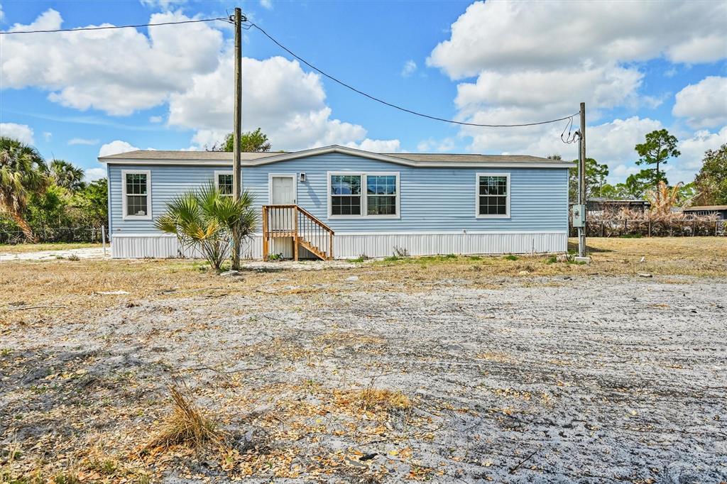 A light blue manufactured home sits on a dirt lot under a blue sky — 1770 TUCKER LANE, NORTH FORT MYERS, FL