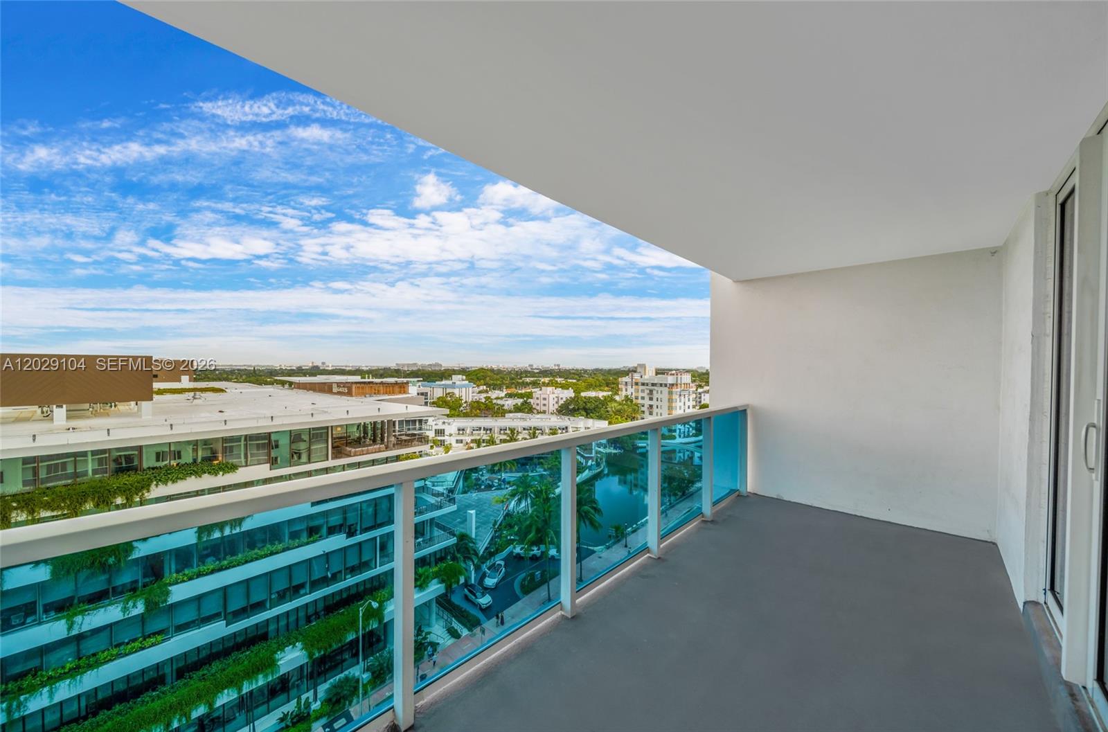 A balcony with a glass railing overlooks a city street and a canal — 2301 Collins Ave # 1030, Miami Beach FL 33139, MIAMI BEACH, FL