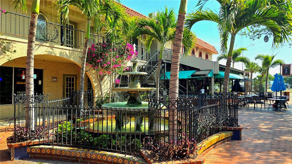 A tiered stone fountain sits in a brick courtyard surrounded by palm trees and buildings — 530 US-41-BYP UNIT 1A, VENICE, FL