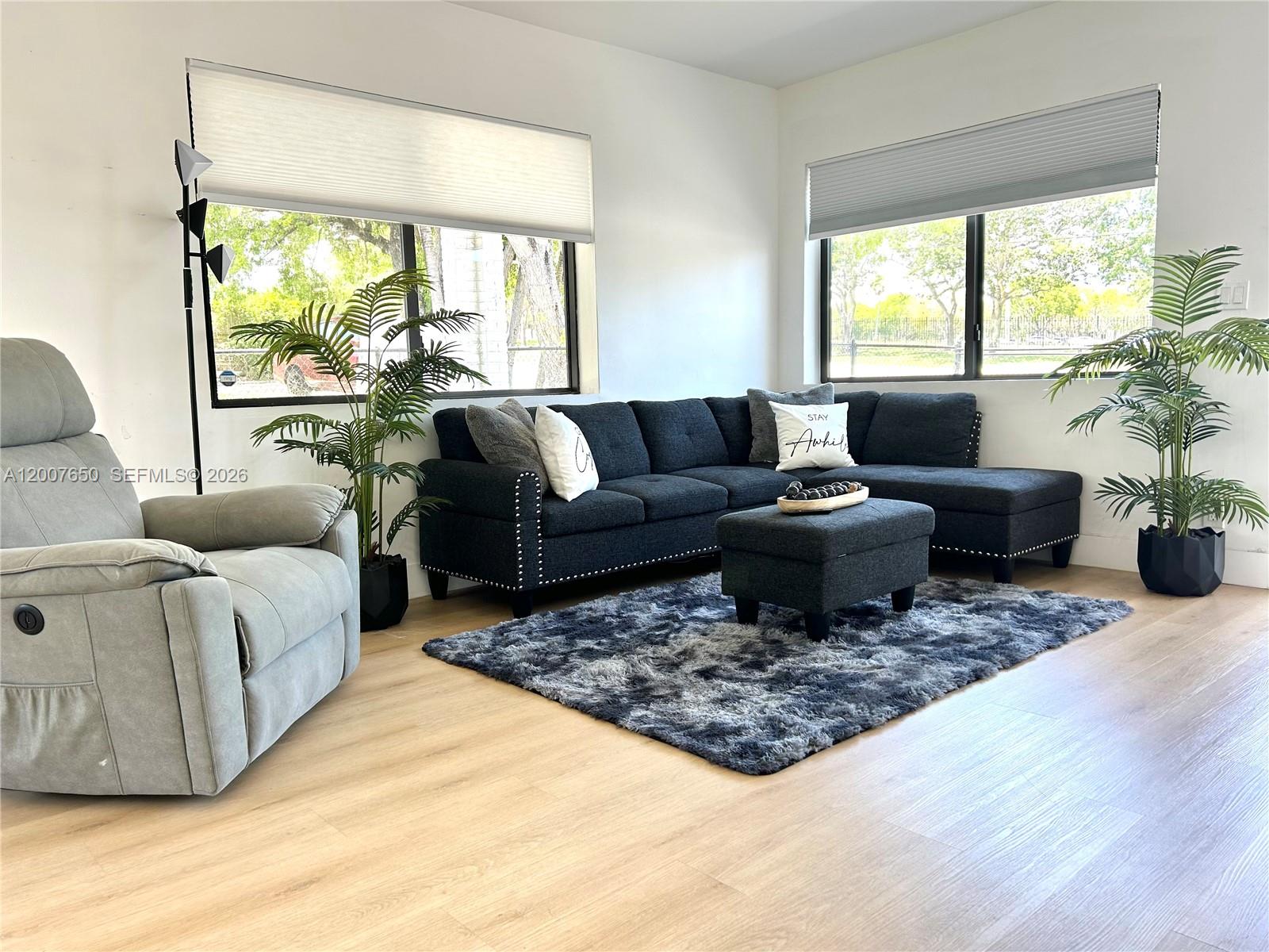 A living room features a dark sectional sofa, a gray recliner, and two potted plants — 808 45th St, West Palm Beach FL 33407, WEST PALM BEACH, FL