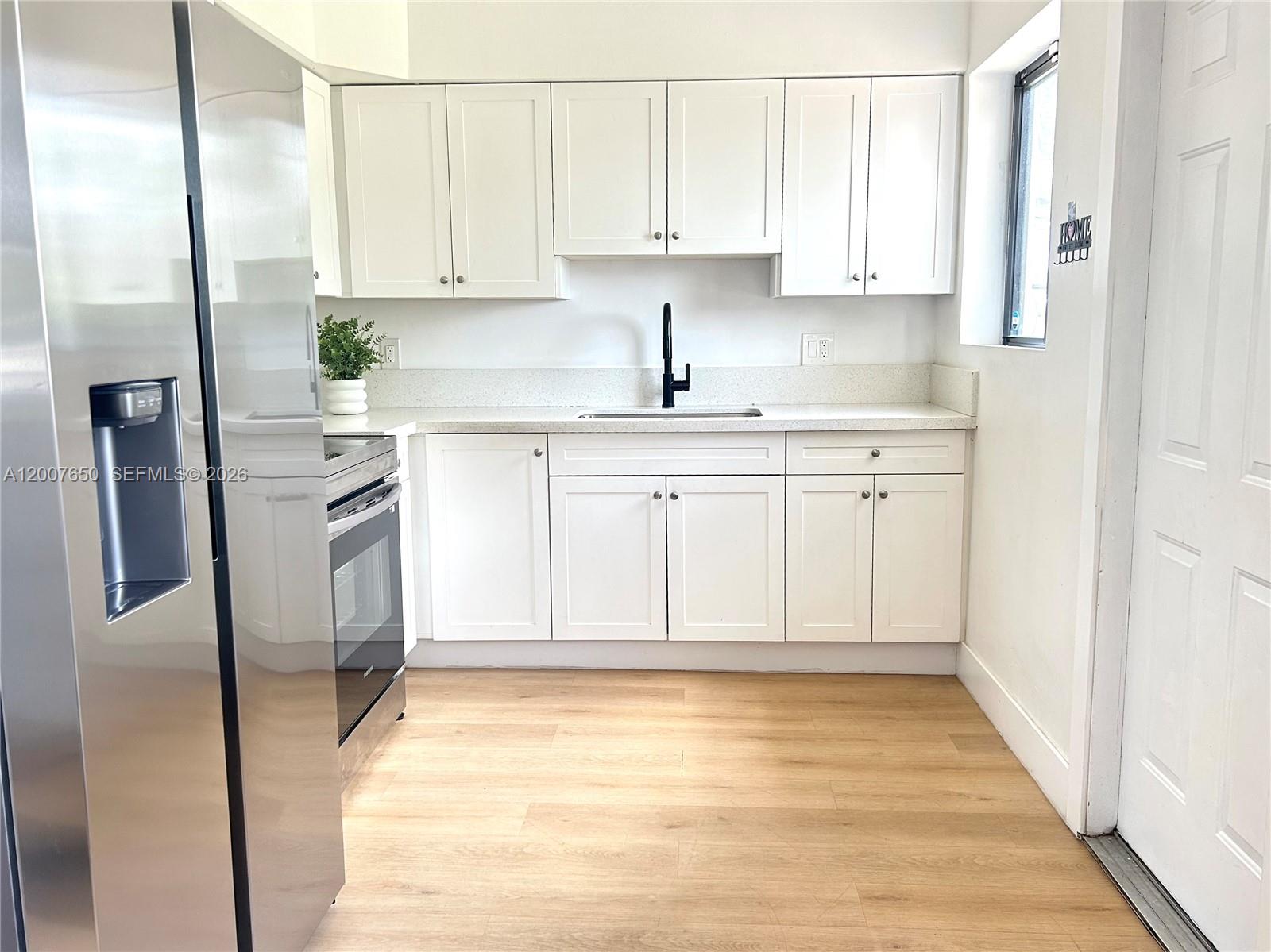 A kitchen features white cabinets, stainless steel appliances, a black faucet, and light wood flooring — 808 45th St, West Palm Beach FL 33407, WEST PALM BEACH, FL