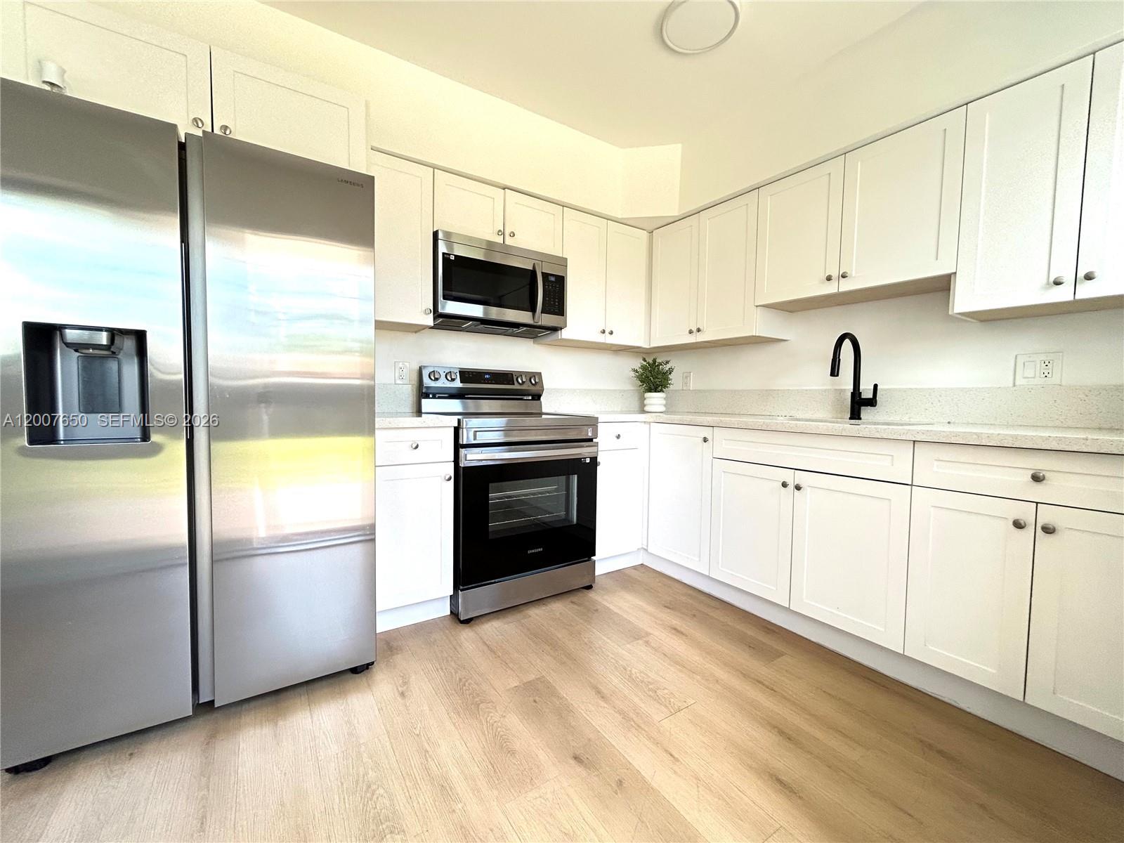 A kitchen features white cabinets, stainless steel appliances, and light wood-look flooring — 808 45th St, West Palm Beach FL 33407, WEST PALM BEACH, FL