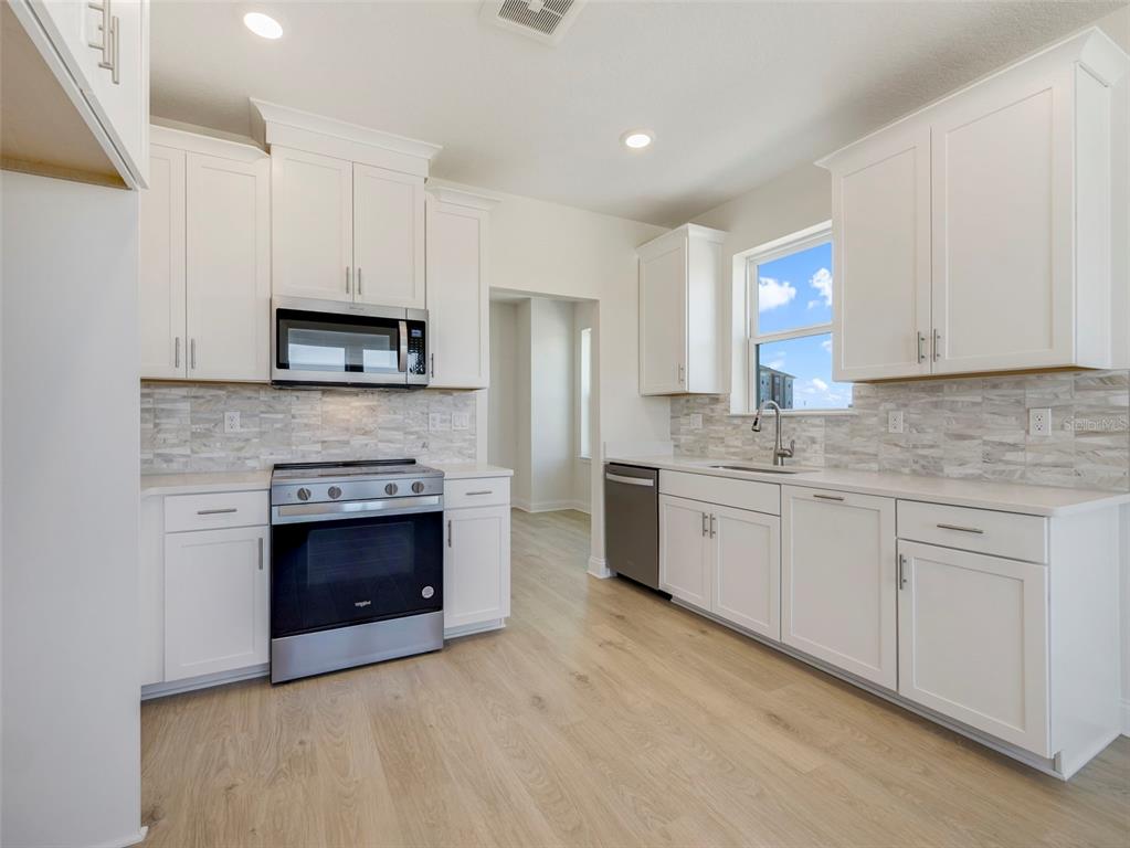 A modern kitchen features white cabinets, stainless steel appliances, light wood flooring, and a tiled backsplash — 7545 LAUREATE BOULEVARD UNIT 7203, ORLANDO, FL
