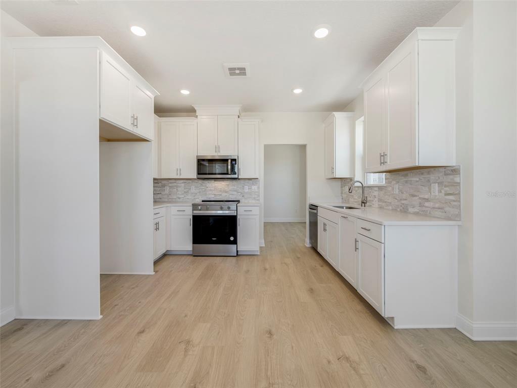 A kitchen features white cabinetry, stainless steel appliances, light wood flooring, and a tiled backsplash — 7545 LAUREATE BOULEVARD UNIT 7203, ORLANDO, FL