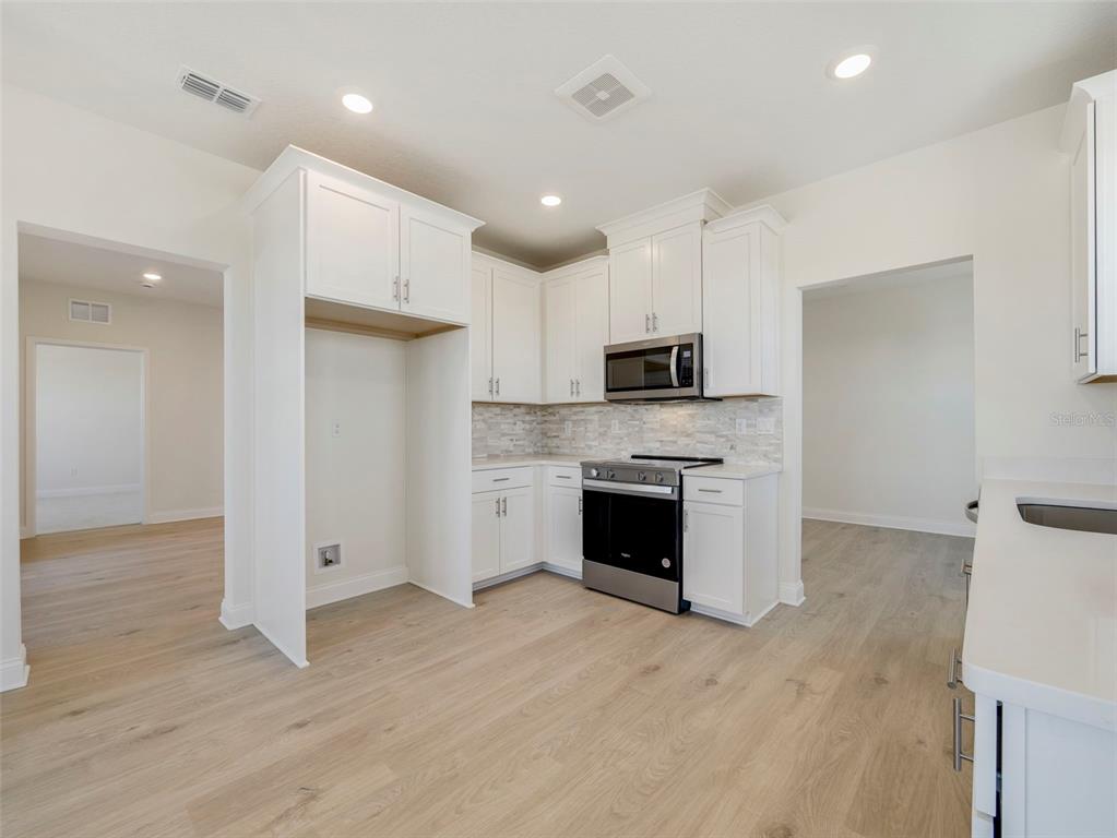 A kitchen features white cabinets, stainless steel appliances, a tiled backsplash, and light wood flooring — 7545 LAUREATE BOULEVARD UNIT 7203, ORLANDO, FL