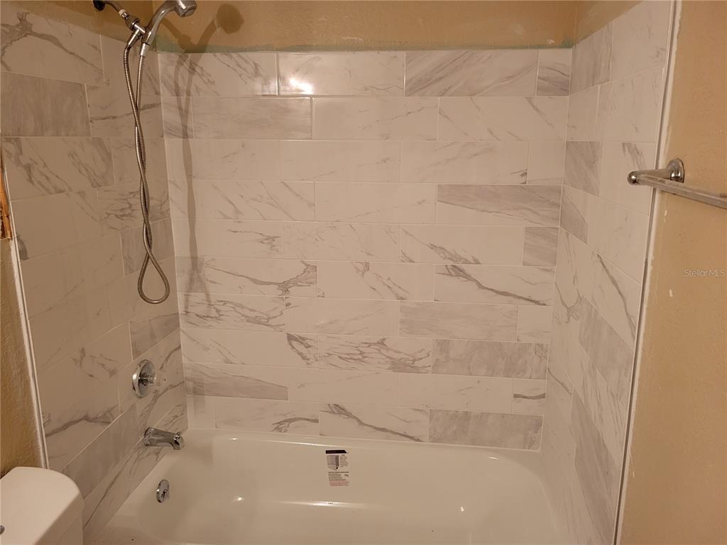A bathtub with a handheld showerhead and white marble-look tile walls in a bathroom — 5635 DEVONBRIAR WAY UNIT K204, ORLANDO, FL